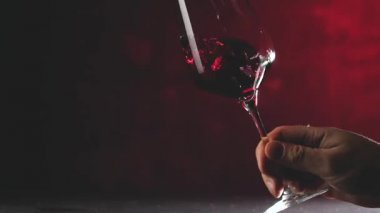 Kırmızı arka planda kırmızı şarapla kırmızı şarabı sallayan birinin kırpılmış görüntüsü.