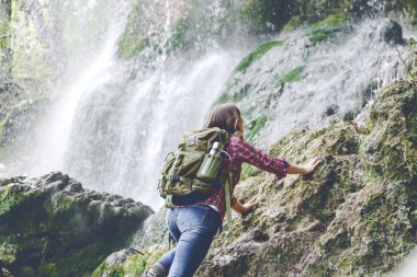 şelale yakınındaki kayaüzerinde tırmanma sırt çantası ile genç kadının arka görünümü