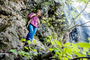 şelale yakınındaki kaya üzerinde duran sırt çantası ile mutlu genç kadının düşük açılı görünümü