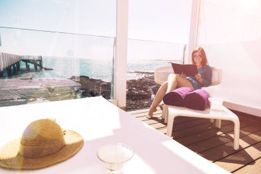 Deniz kenarında otururken kitap okuma güneş gözlüklü genç kadın