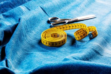 denim kumaş üzerinde sarı ölçüm bandı ve makas yakın çekim görünümü, dikiş arka plan  