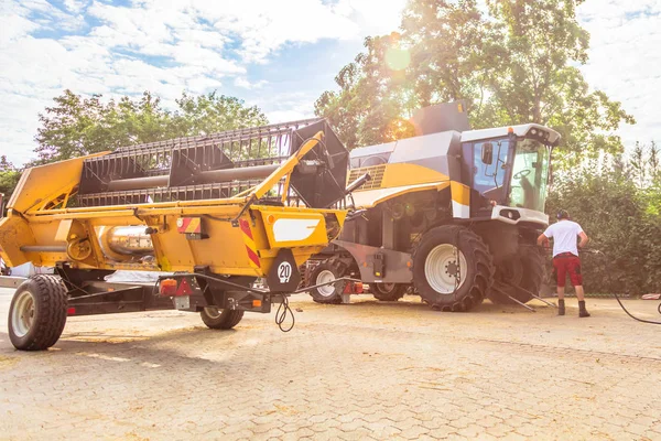 mechanic repairing the yellow and green combine harvester in the farm yard.