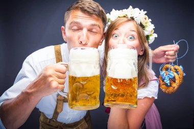 Genç adam ve kadın ellerinde bira içip kameraya bakıyorlar, Ekim Festivali konsepti.