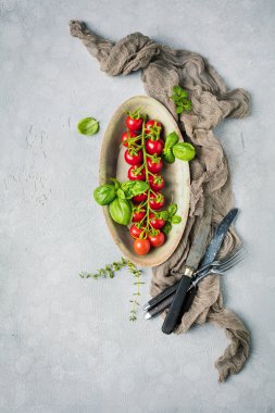 taze olgun kiraz domates üst görünümü, tabakta fesleğen yaprakları ve gri yüzeyde çatal 