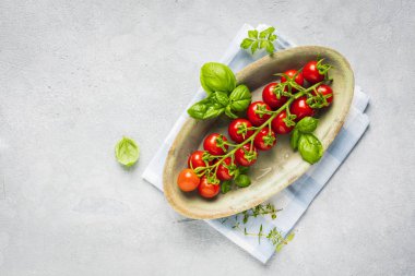 taze olgun kiraz domates ve fesleğen yaprakları gri yüzeyüzerinde tabakta üst görünümü