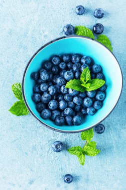 mavi arka plan üzerinde kase yaprakları ile taze olgun sağlıklı yaban mersini üst görünümü