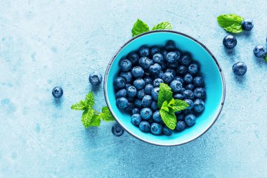 mavi arka plan üzerinde kase yaprakları ile taze olgun sağlıklı yaban mersini üst görünümü