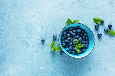 mavi arka plan üzerinde kase yaprakları ile taze olgun sağlıklı yaban mersini üst görünümü