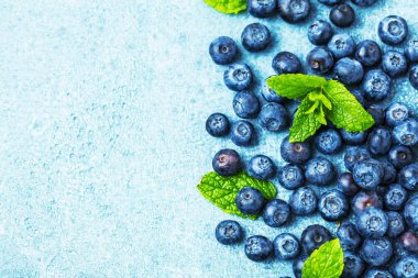 Mavi zemin üzerinde nane yaprakları olan taze olgun yaban mersinlerinin üst görüntüsü