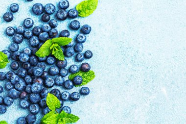 Mavi zemin üzerinde nane yaprakları olan taze olgun yaban mersinlerinin üst görüntüsü