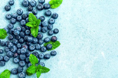 Mavi zemin üzerinde nane yaprakları olan taze olgun yaban mersinlerinin üst görüntüsü