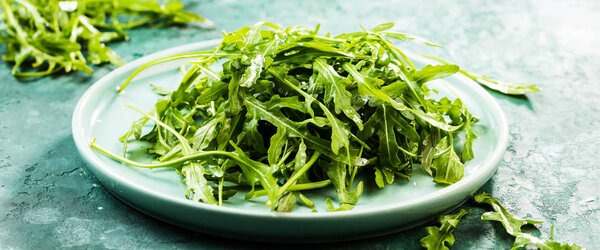 close-up view of fresh arugula leaves on plate on rustic background