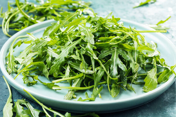 close-up view of fresh arugula leaves on plate on rustic background