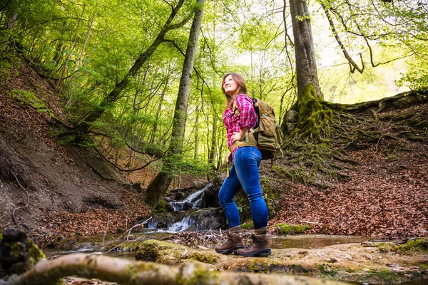 low angle view of beautiful smiling young woman with backpack hiking in forest