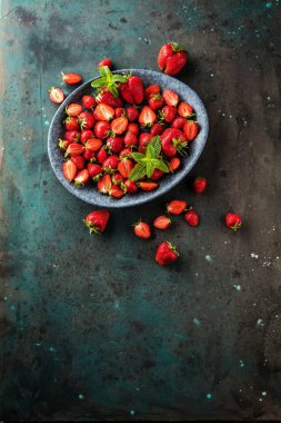 taze olgun çilek ve yeşil yaprakları gri arka planda kase üst görünümü
