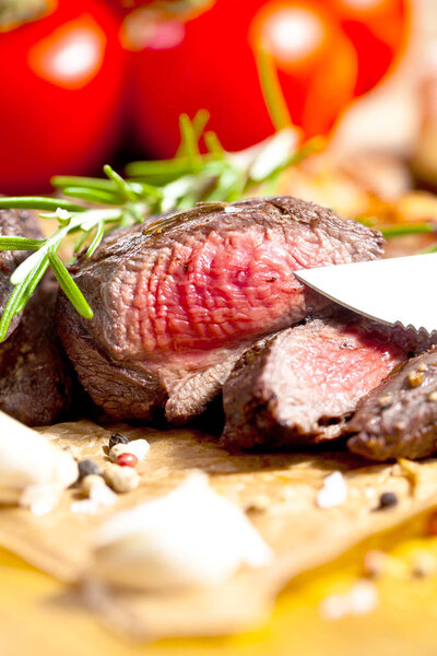 Close-up view of delicious grilled venison steak with rosemary, garlic, spices and tomatoes on table