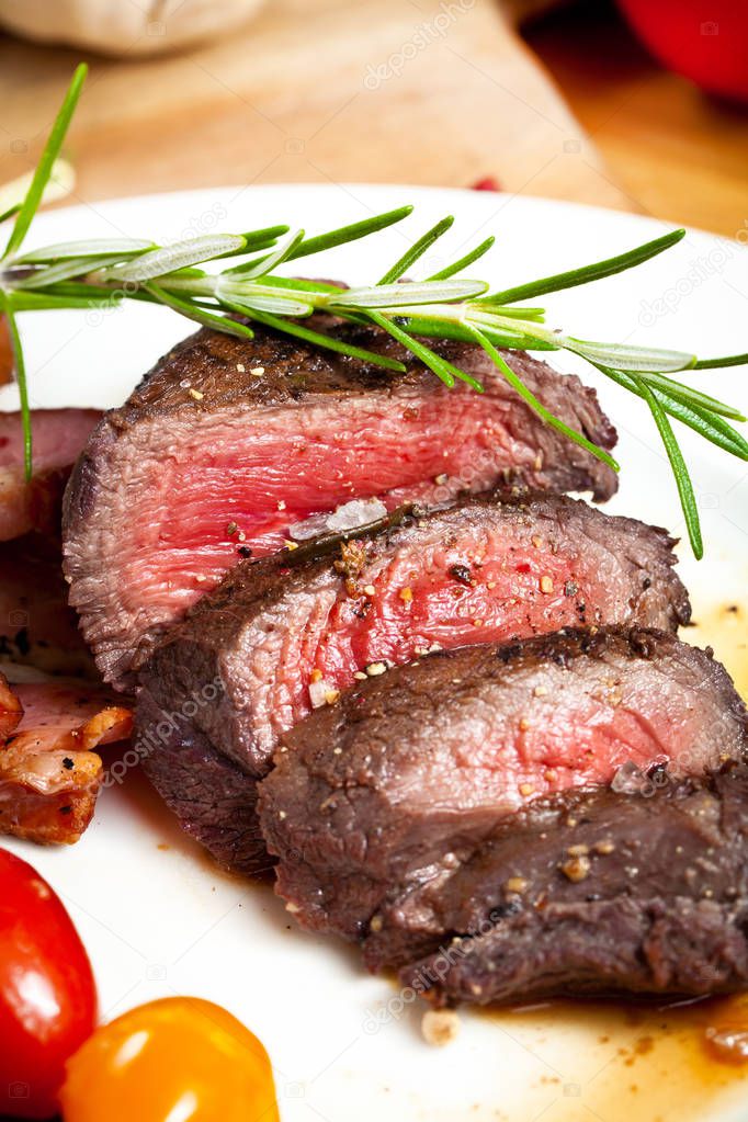 grilled venison steak with rosemary, spices and tomatoes on plate