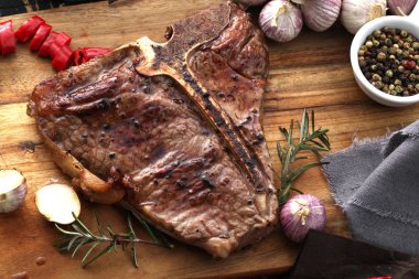 Ahşap bir tahta da servis edilen baharatlar ve taze otlar ile ızgara T-bone biftek yakın çekim görünümü 