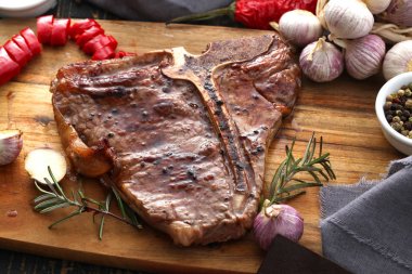 Ahşap bir tahta da servis edilen baharatlar ve taze otlar ile ızgara T-bone biftek yakın çekim görünümü