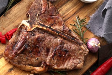 Ahşap bir tahta da servis edilen baharatlar ve taze otlar ile ızgara T-bone biftek yakın çekim görünümü