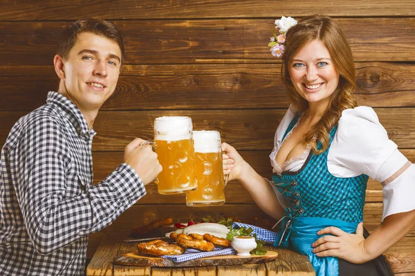 ビールのグラスを持ち おいしい食事でテーブルに座っている間 カメラで微笑む若いカップル — ストック写真