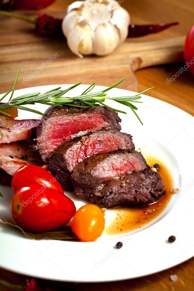 grilled venison fillet with tomatoes, rosemary, peppers and garlic on wooden table