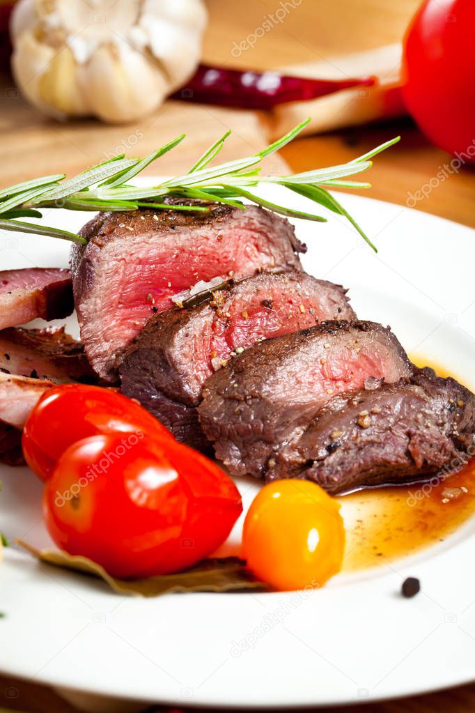 grilled venison fillet with tomatoes, rosemary, peppers and garlic on wooden table