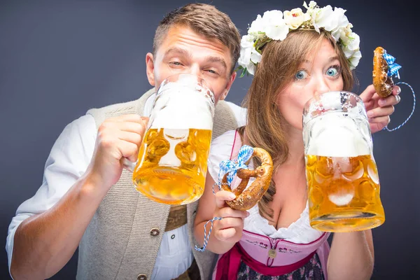 プレッツェルを持ち 灰色で隔離されたビールを飲む幸せな若いカップル — ストック写真