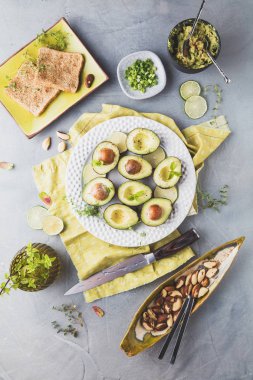 gri yüzeyde taze avokado, Limes, tost, otlar ve fındık üst görünümü