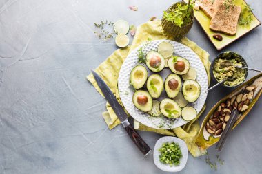 gri yüzeyde taze avokado, Limes, tost, otlar ve fındık üst görünümü