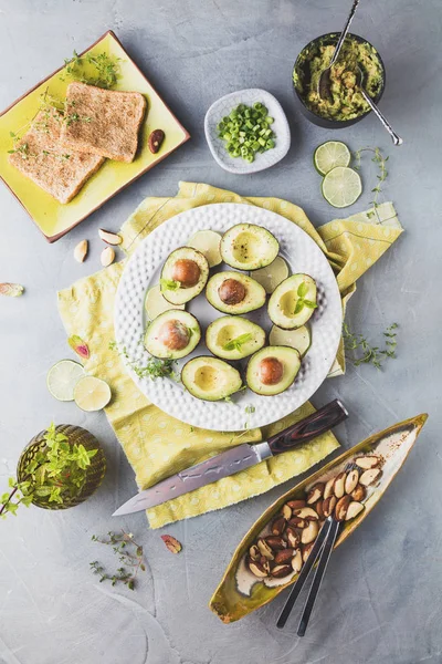 gri yüzeyde taze avokado, Limes, tost, otlar ve fındık üst görünümü