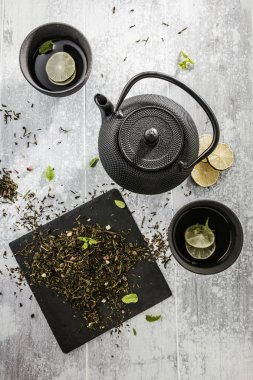 çay, bardak ve gri yüzeyde dilimlenmiş limon ile siyah çaydanlık üst görünümü