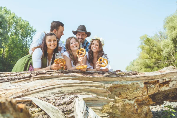 快乐的年轻朋友在巴伐利亚的服装拿着啤酒与薄饼和微笑在相机户外 — 图库照片