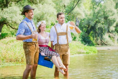 mutlu genç erkekler bira bardak tutan ve dirndl içinde kız taşıyan kutu açık oturan