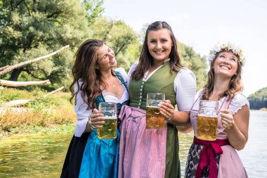 Bavyera kostümlü mutlu bayan arkadaşlar ellerinde bira bardakları açık havada eğleniyorlar.