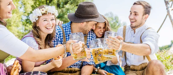 快乐的年轻朋友在巴伐利亚服装闪烁的啤酒杯户外 — 图库照片