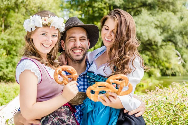 穿着巴伐利亚服装的快乐朋友们手握椒盐卷饼 在户外玩得很开心 — 图库照片