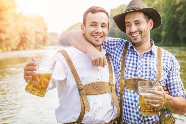 バイエルンの衣装を着た幸せな男性の友人がビールグラスを持って屋外で一緒に楽しみ — ストック写真