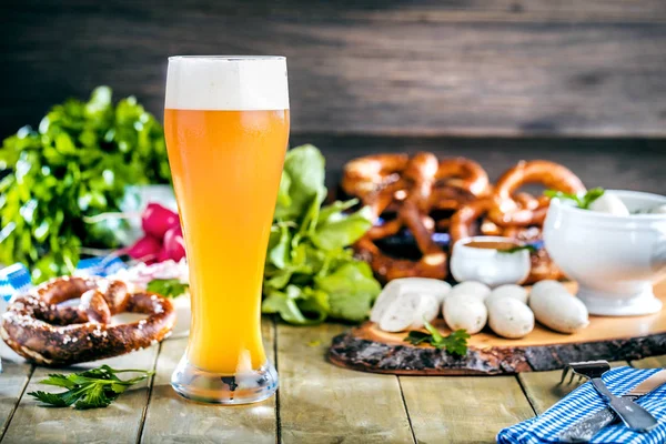 glass of beer, pretzels, vegetables and sausages on wooden table