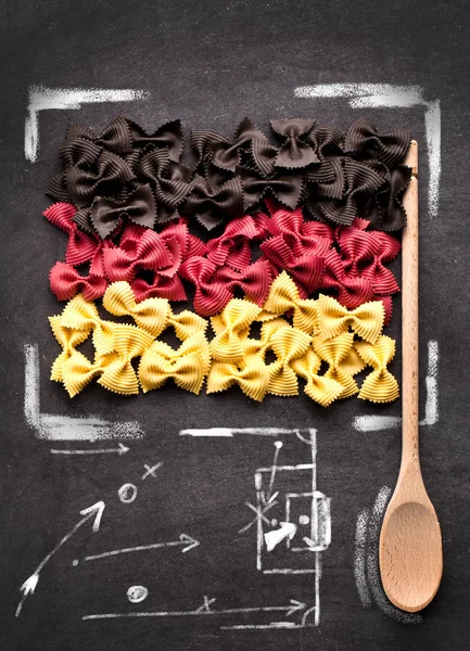 top view of uncooked pasta in colors of german flag and wooden spoon on black background