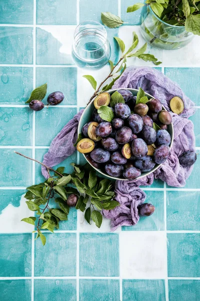 Topputsikt Över Färska Mogna Plommon Skål Och Gröna Blad Bordet — Stockfoto