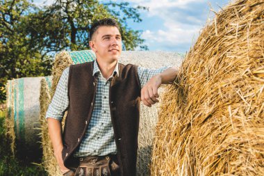 samanlıkta yaslanan geleneksel Alman kostümlü yakışıklı genç adam 