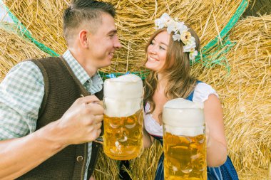 geleneksel Bavyera kostümleri mutlu genç çift saman balyaları, oktoberfest kavramı yakınında birlikte bira içme 