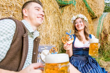 mutlu genç çift simit yeme ve saman balyaları, oktoberfest kavramı yakınında otururken bira içme 
