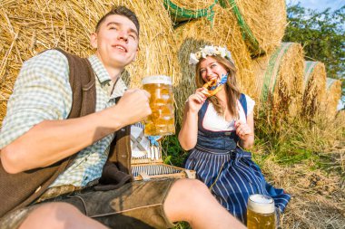 mutlu genç arkadaşlar simit yeme ve saman balyaları, oktoberfest kavramı yakınında otururken bira içme