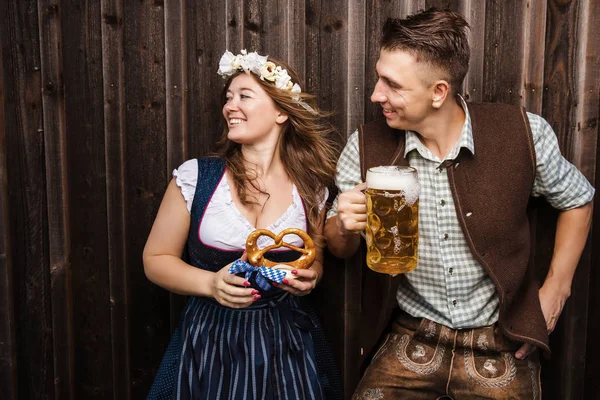 ビールとプレッツェルを持つバイエルンの衣装を着た若いカップル オクトーバーフェストコンセプト — ストック写真