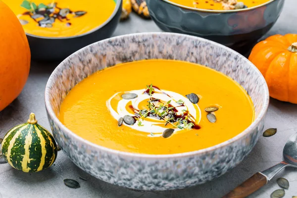 close-up view of fresh pumpkin soup in bowls and whole pumpkins on table