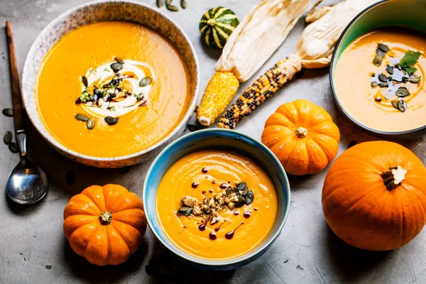 top view of fresh pumpkin soup in bowls and whole pumpkins on table