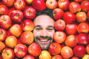 Man with red apples, concept for food industry. Face of grimacing man in apples area  clipart