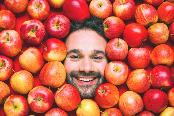 Man with red apples, concept for food industry. Face of grimacing man in apples area 